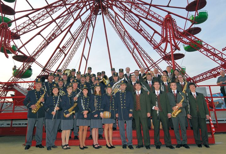Gruppenfoto zweier Kapellen in Uniform vor einem roten Riesenrad beim Projekt „Höhenrausch“, Linz09