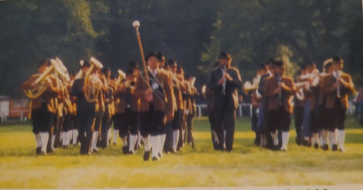 Die Kapelle marschiert in Tracht über eine Wiese, vorne der Stabführer, Rastede 1984