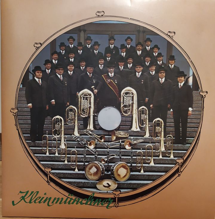 Schallplattencover „Kleinmünchner“ von 1976: die Kapelle in dunklen Anzügen und Hüten auf einer Treppe, davor Blechblasinstrumente und Trommeln